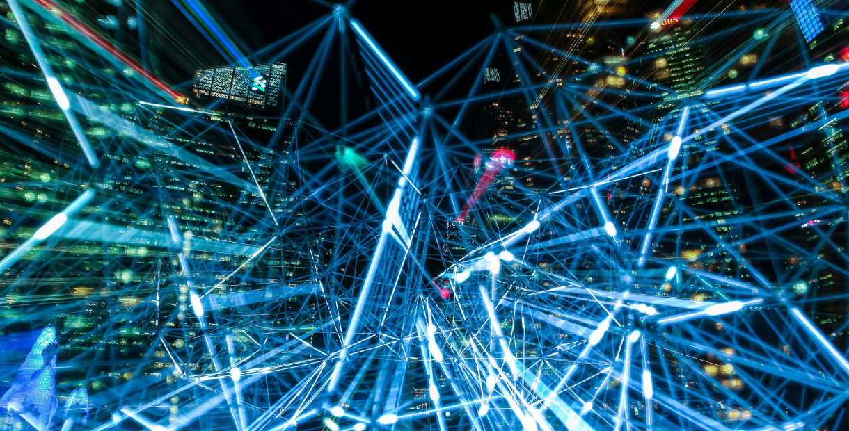 Abstract digital illustration of a city skyline at night overlaid with glowing blue interconnected lines and nodes, representing artificial intelligence, digital networks, data connections, and modern search technology. Bright light trails and illuminated buildings create a futuristic technology-focused scene.